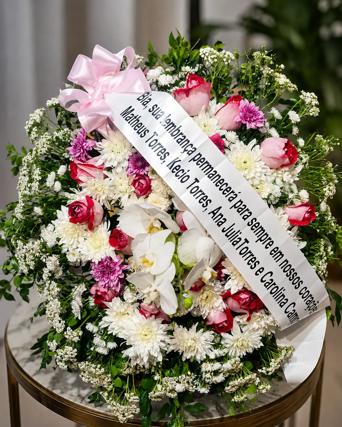 Coroa de flores brancas e rosas com faixa de homenagem